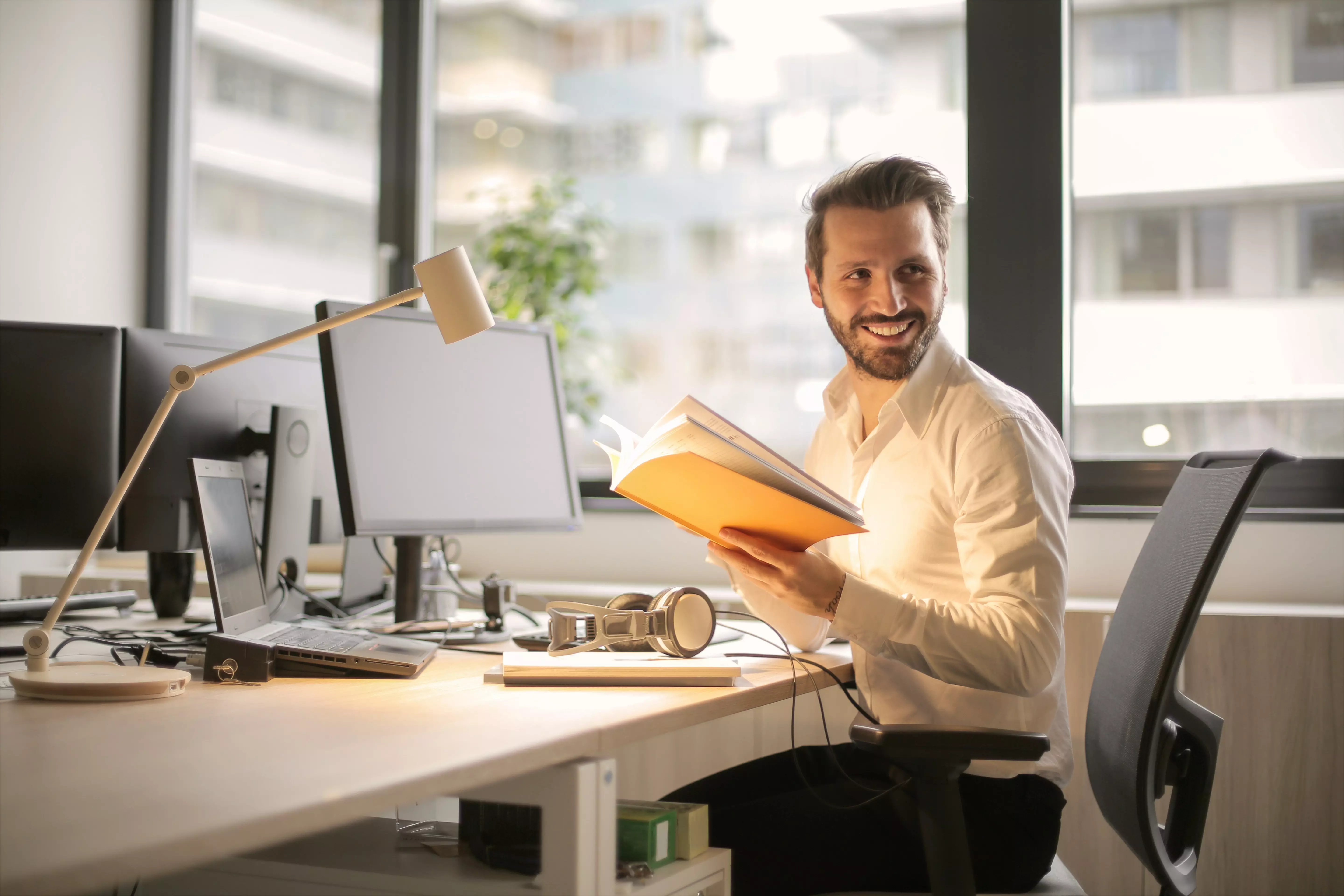 Smiling man sitting at his workplace with a book in his hand.