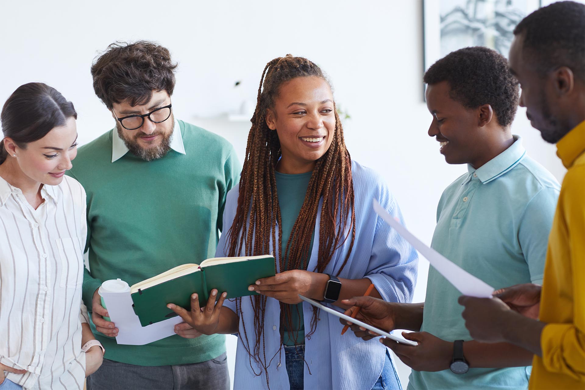 Ofereça diversas oportunidades de aprendizagem para reduzir o fenómeno da desistência silenciosa. Nesta imagem, um retrato da cintura para cima de uma equipa empresarial multiétnica a ouvir uma mulher afro-americana sorridente durante uma reunião no escritório.