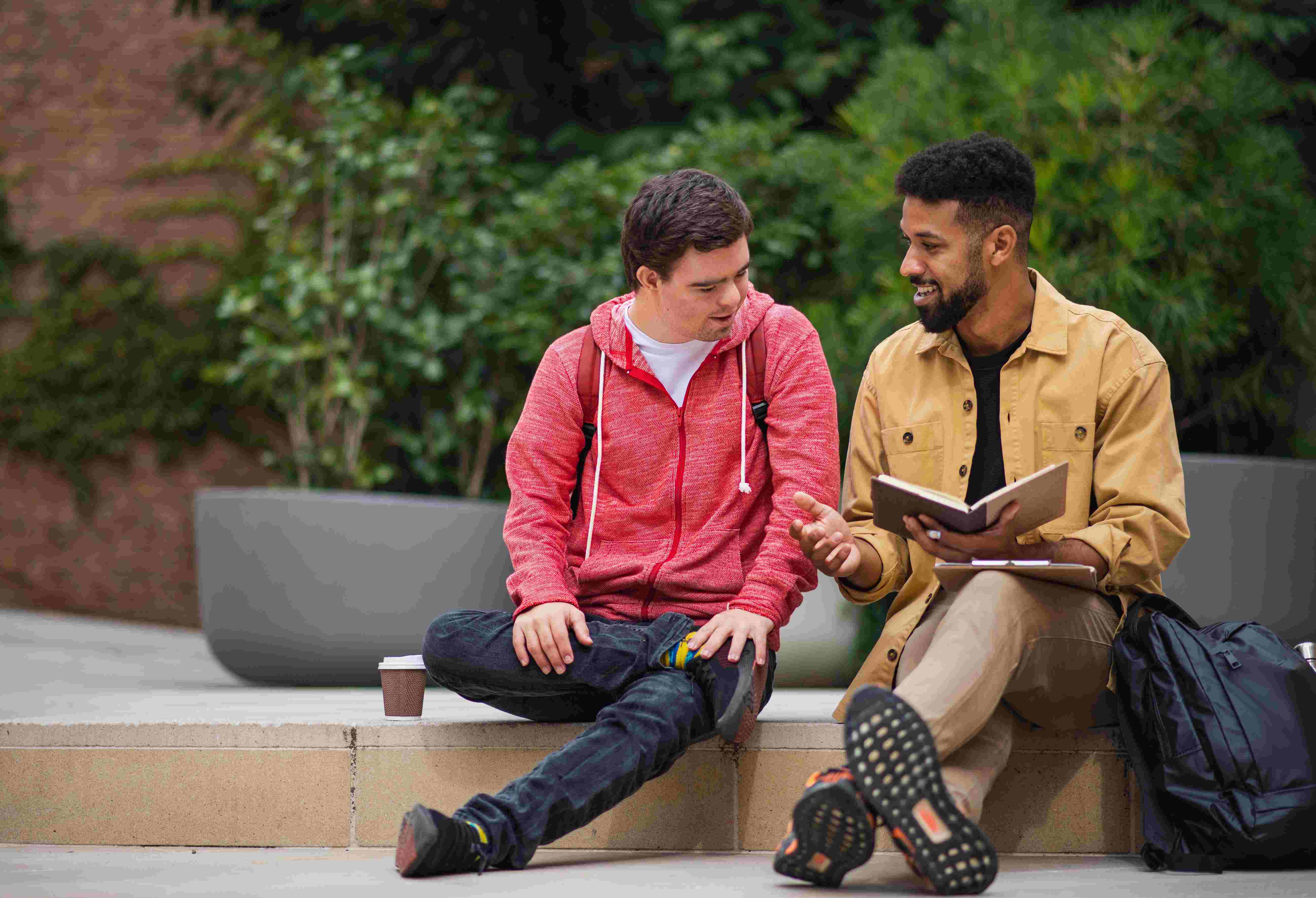 Ofereça oportunidades de aconselhamento profissional personalizado para reduzir o fenómeno da desistência silenciosa. Nesta imagem, um jovem feliz com síndrome de Down e um amigo mentor sentados e a conversar ao ar livre